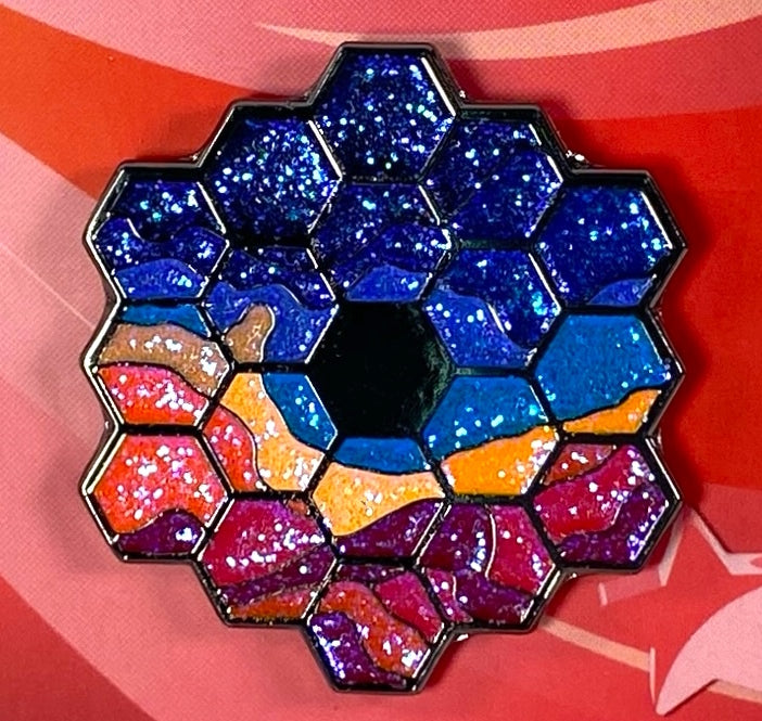 Soft enamel pin depicting the Cosmic Cliffs as viewed through the mirrored lens of the James Web Telescope, the glitter serving to capture the beauty of a million million twinkling stars.